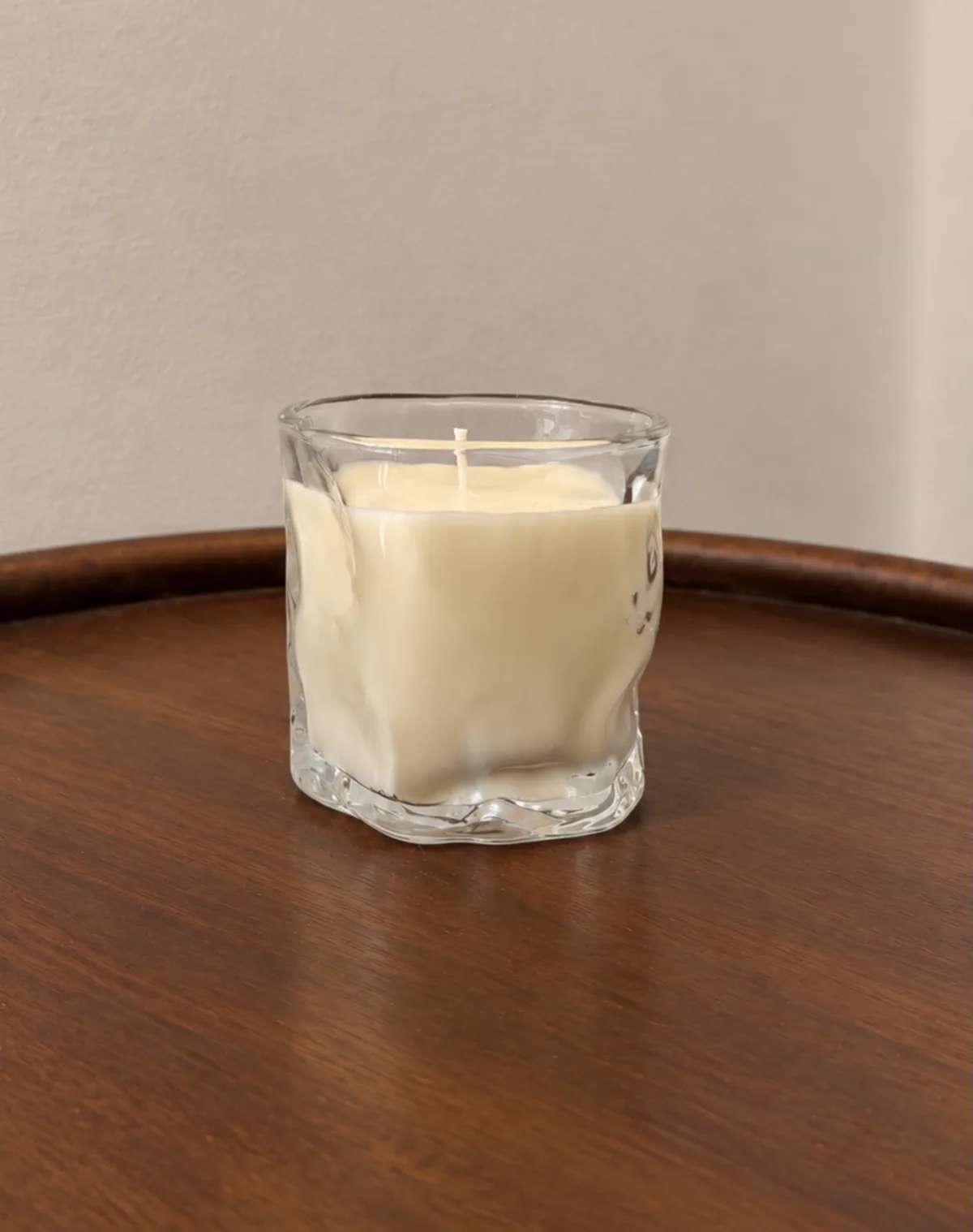 Vela en vaso de vidrio de forma irregular, sobre una mesa de madera