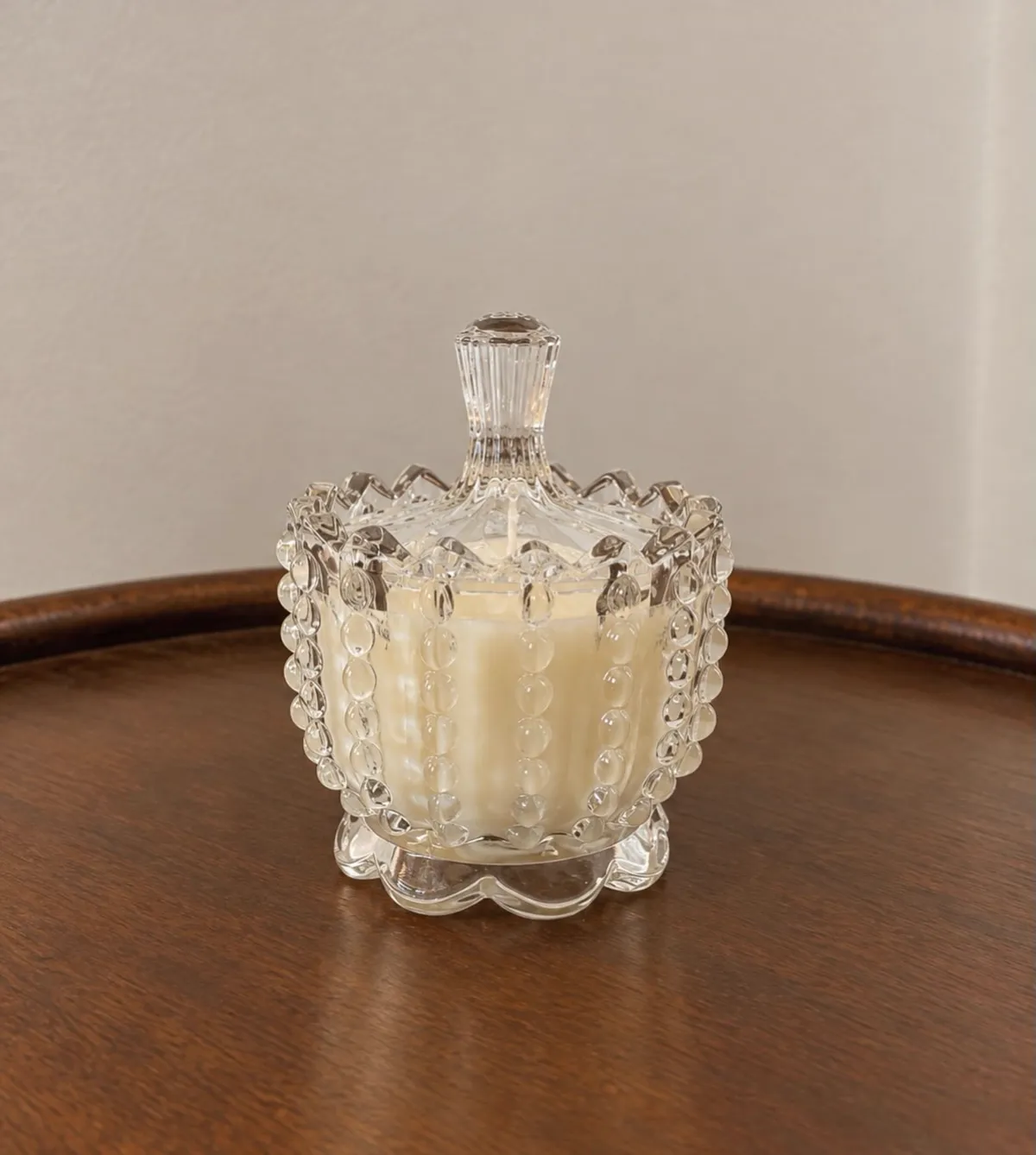 Vela en vaso de cristal tallado con tapa, sobre una mesa de madera