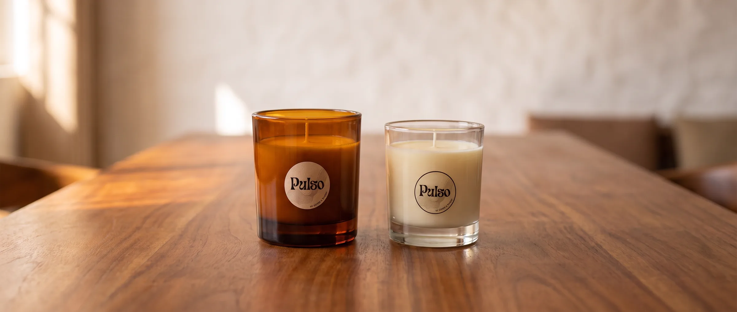Dos velas Pulso, una en vaso ámbar y otra en vaso transparente, sobre una mesa de madera